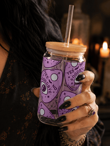 Woman holding a purple Ouija-inspired 20oz glass can with bamboo lid in a cozy witchcore home, showcasing Haus of Moggie's alternative drinkware collection.