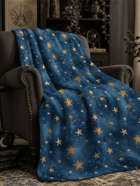 Blue celestial fleece blanket with gold stars draped over a cozy reading chair in a dark academia living room, part of the Spellwoven Collection by Haus of Moggie
